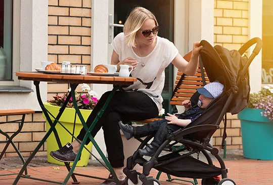Mamma fikar vid cafebord med barn som är ledsen i vagn bredvid
